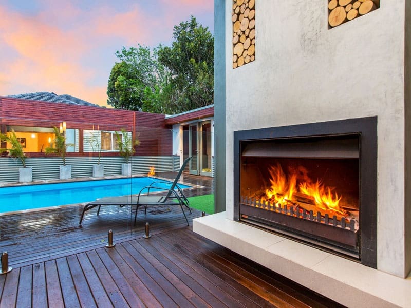 frameless glass pool fence with merbau timber decking and outdoor fireplace in melbourne outdoor entertaining area
